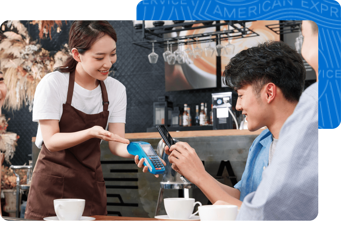  A man in a coffee shop uses his American Express Card on his phone to pay his bill.