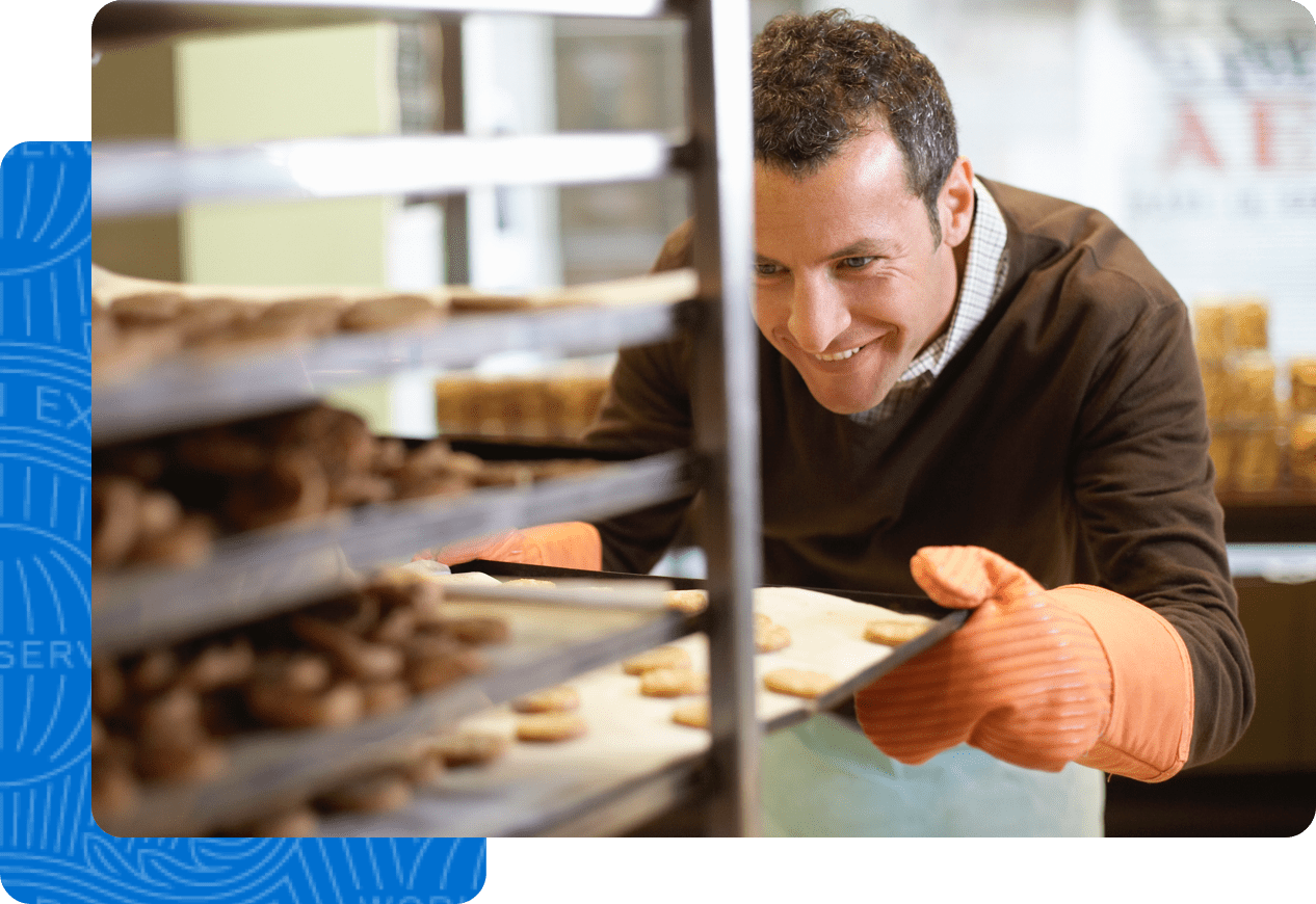 Baker is pulling out a tray of cookies and is getting ready to open his business for the day. 