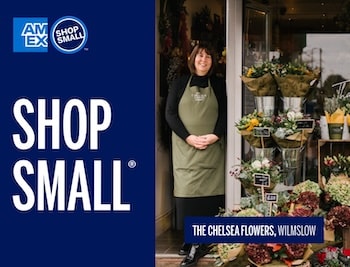 Plant store owner standing in storefront entrance with Shop Small sign