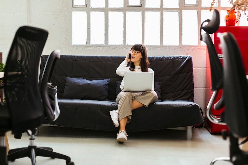 Business woman sitting on couch with laptop talking on the phonne