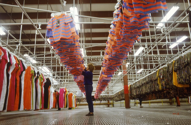 Woman working at a garment factory checking a row of orange and blue t-shirts.