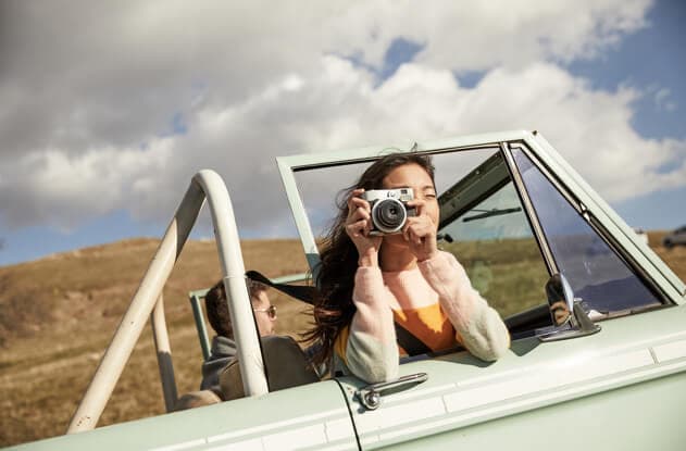 Woman aims her camera through passenger side car window.