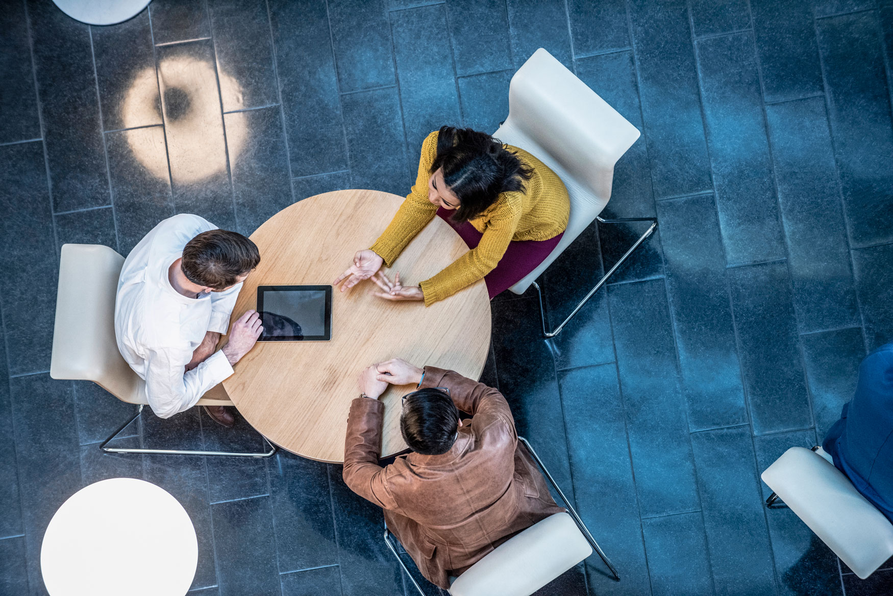 Overhead view of a small group of corporate business people at a round desk using a digital tablet, discussing business.