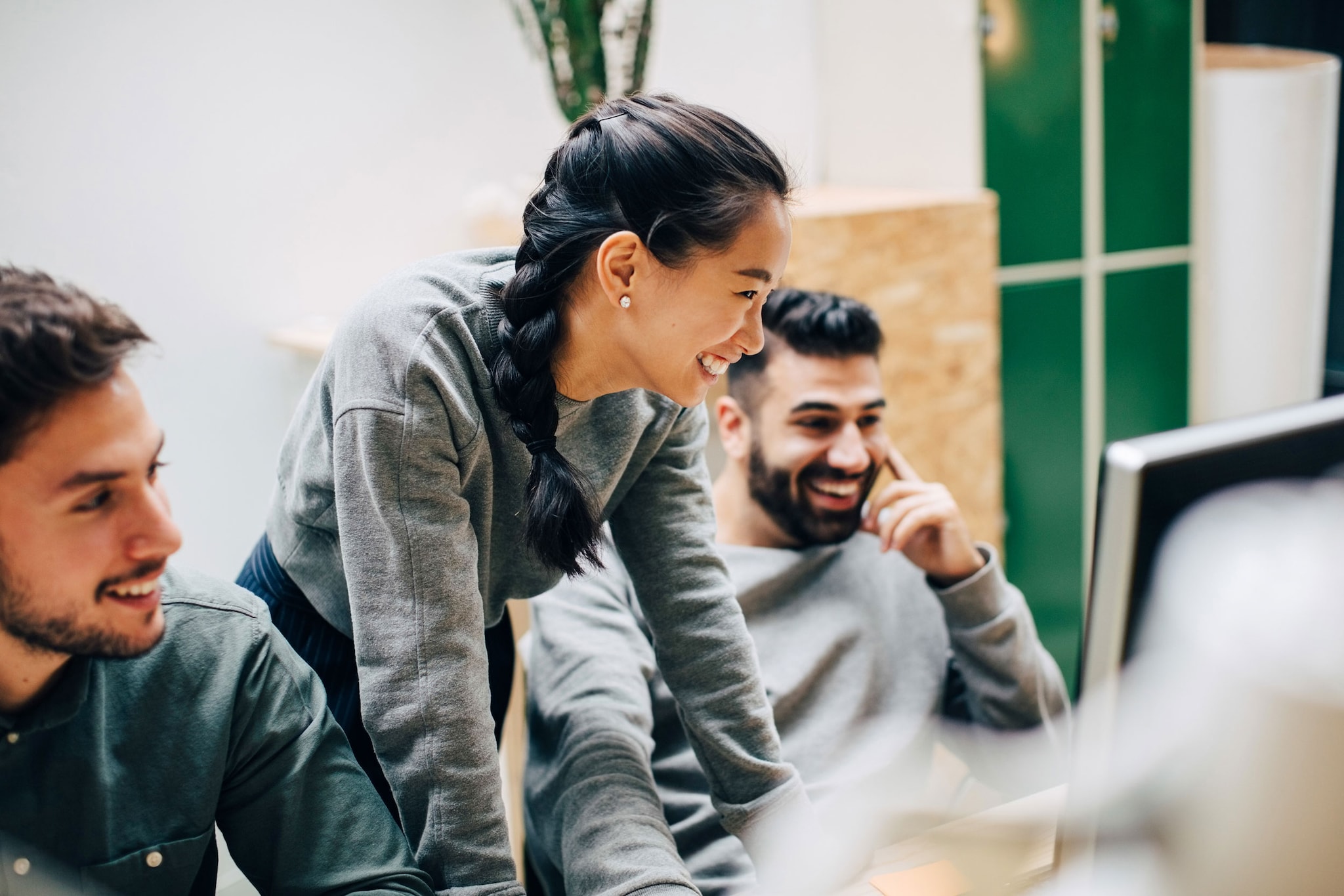 A group of colleagues smiling while discussing what they are seeing on their computer.