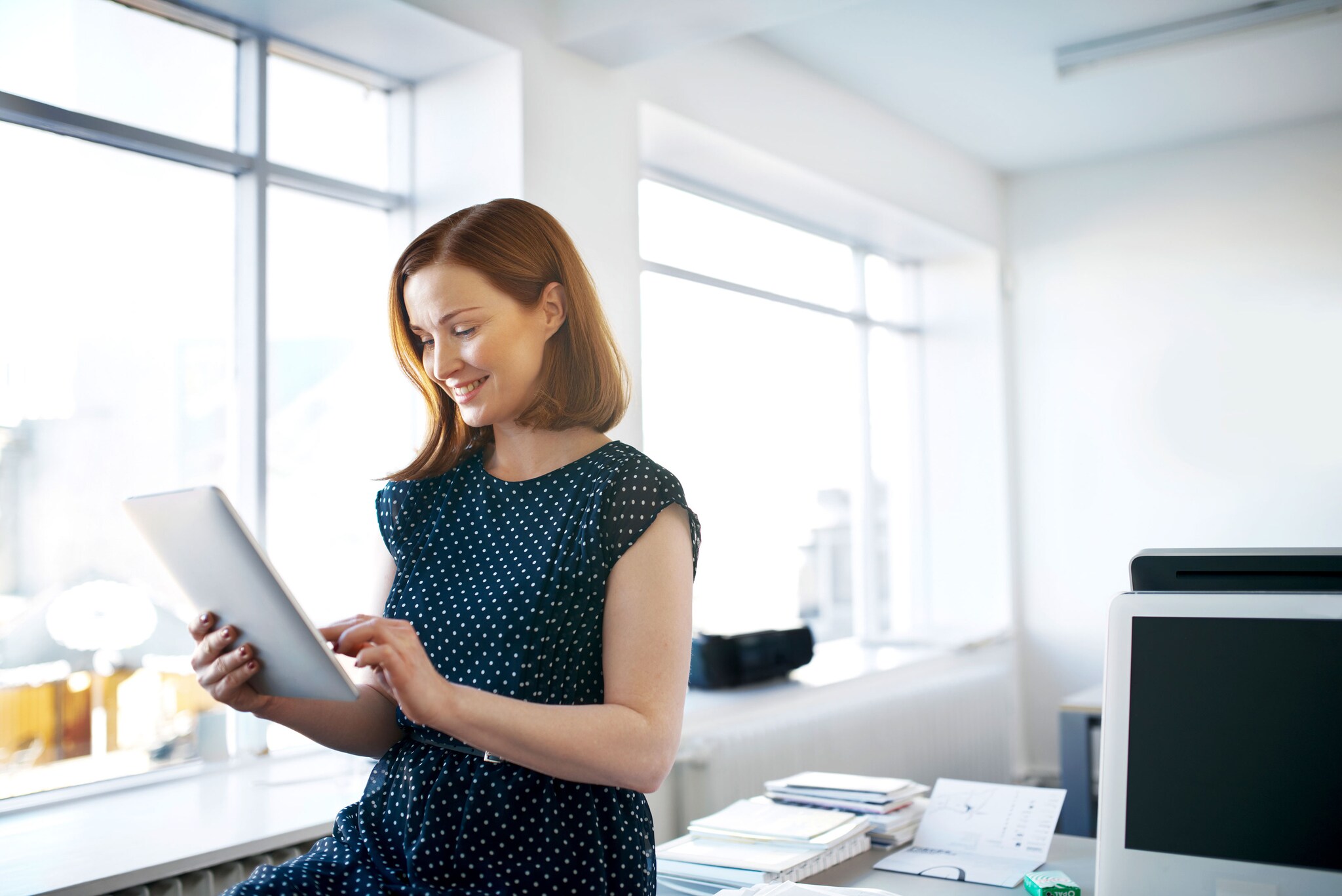 Business woman sitting on a desk reading a digital tablet at her office