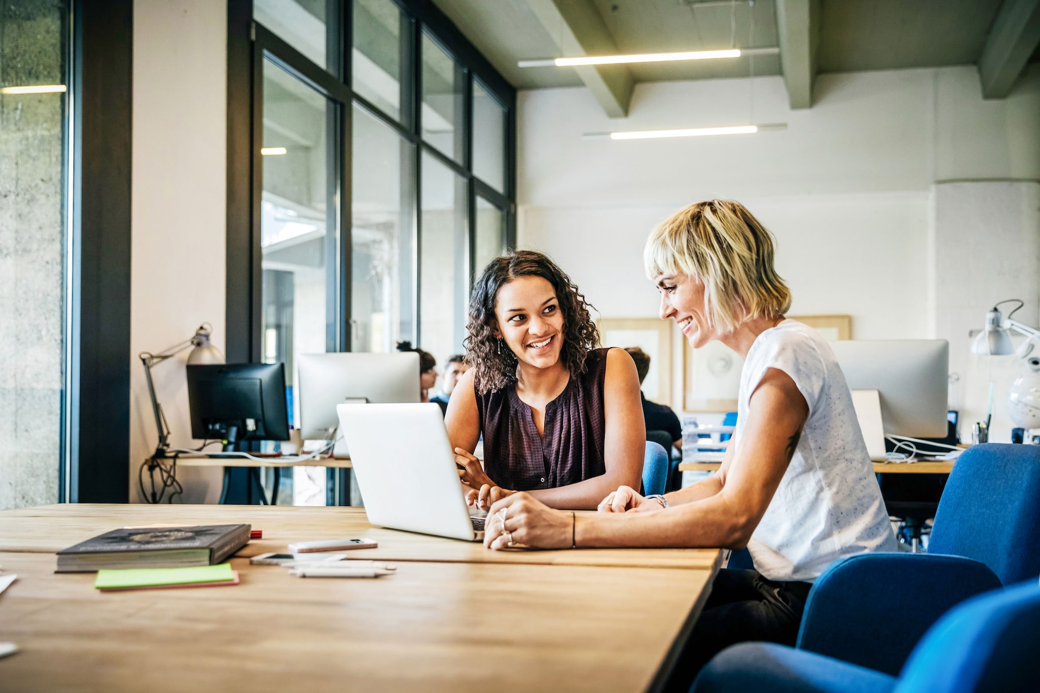 Two casually dressed, start-up businesswomen talking in a meeting with laptop