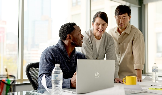 Three coworkers talking in an office while looking at a laptop