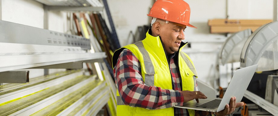 Man in a hard hat and safety vest working on laptop