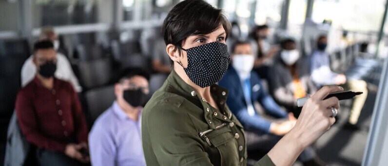 person in front of room writing on board while wearing a mask