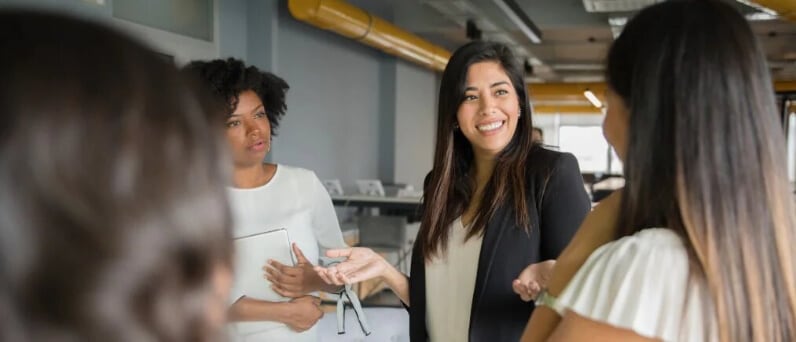 Latina women in office standing in circle and talking