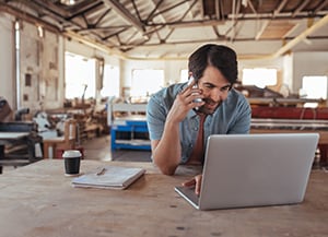 person in warehouse looking at laptop while talking on the phone