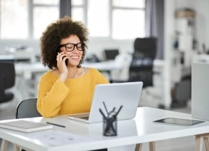 person sitting at desk looking at laptop while talking on the phone