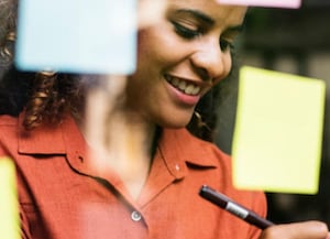 woman writing on post it note and looking at glass wall