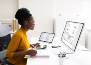 Person sitting at desk with calculator looking at desktop monitor