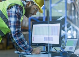 Construction person looking at laptop and standing at desk with monitor