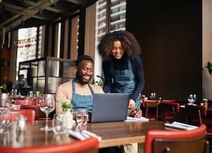 Man and woman in a restaurant looking at a laptop