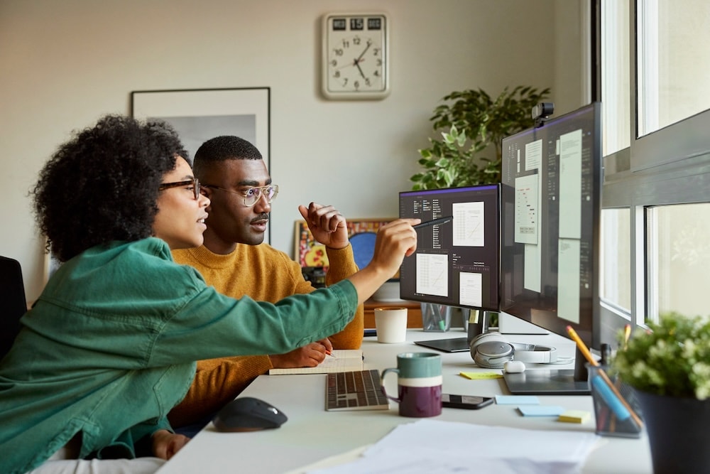 Two people sitting at desk looking at data on computer monitor