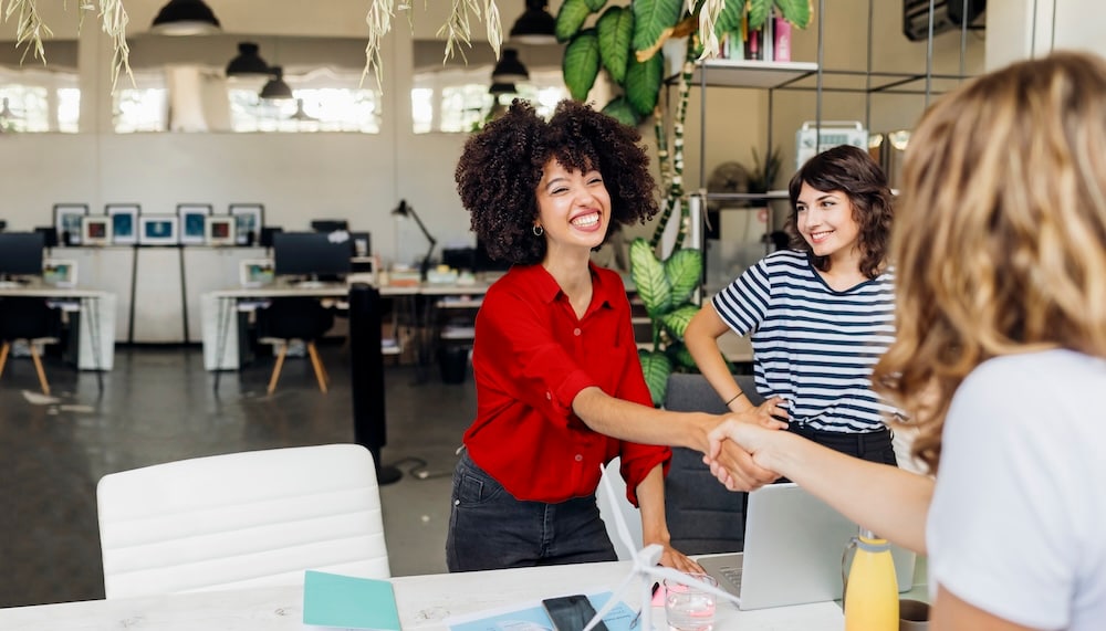 Two women shaking hands over a desk