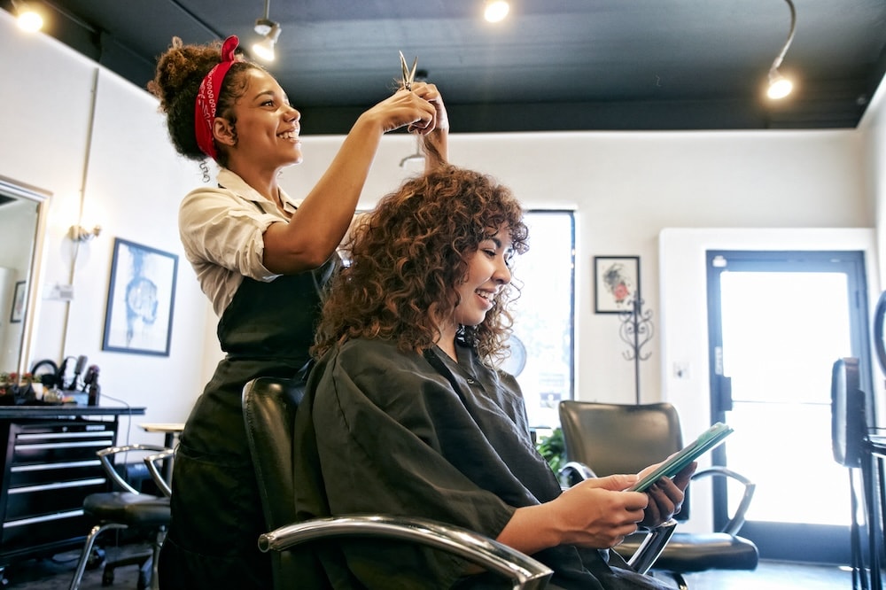 hairdresser cutting a woman's hair, while client looks at tablet