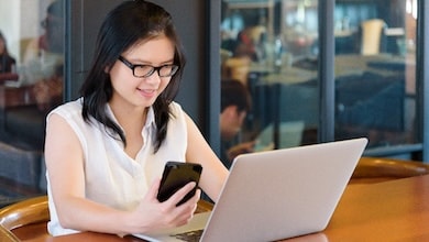 Woman sitting at desk with laptop holding phone