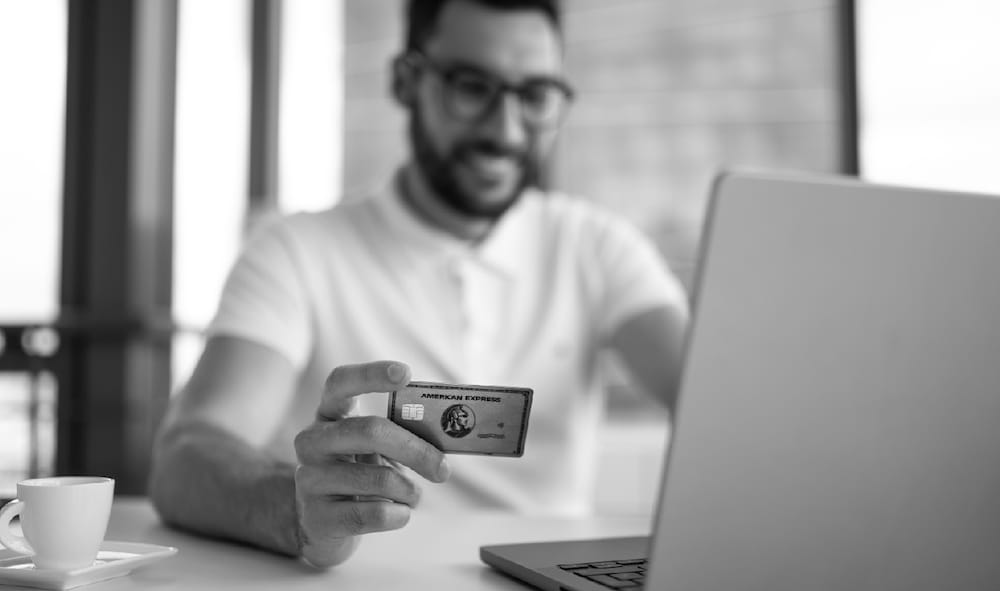 man sitting at table looking at laptop holding American Express card