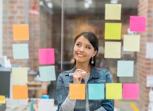Person looking at glass window with post-it notes during brainstorming session