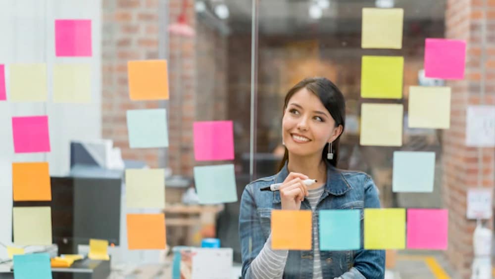 Person looking at glass window with post-it notes during brainstorming session