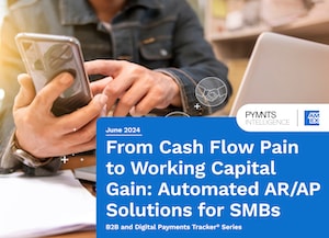 Hand holding smartphone at a desk with laptop