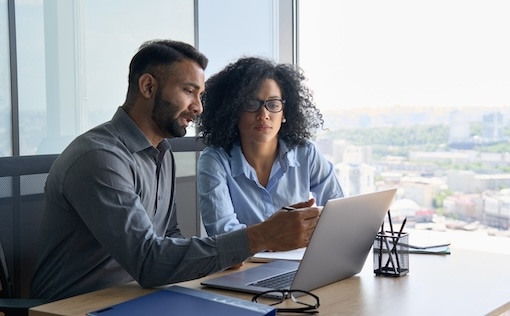 Two people at a desk looking at laptop
