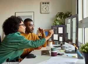 Two people looking at a computer monitor at at desk