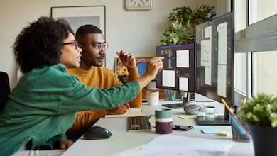 Two people sitting at a desk looking at computer monitor