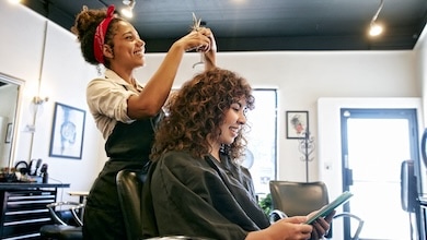 A women getting her hair cut in salon while looking at mobile device