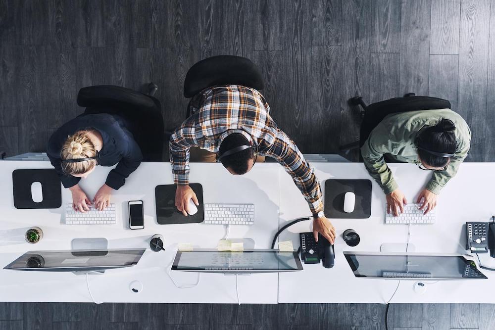 overhead view of three people at long desk typing on computer and answering calls