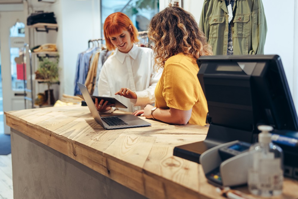 Two women working at a retail counter on a laptop and tablet