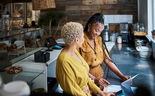 Two women standing behind restaurant counter looking at papers
