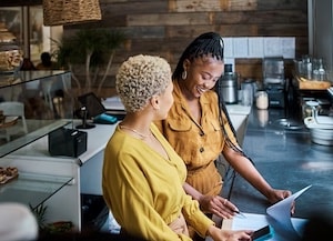 Two women looking at paperwork together behind restaurant counter