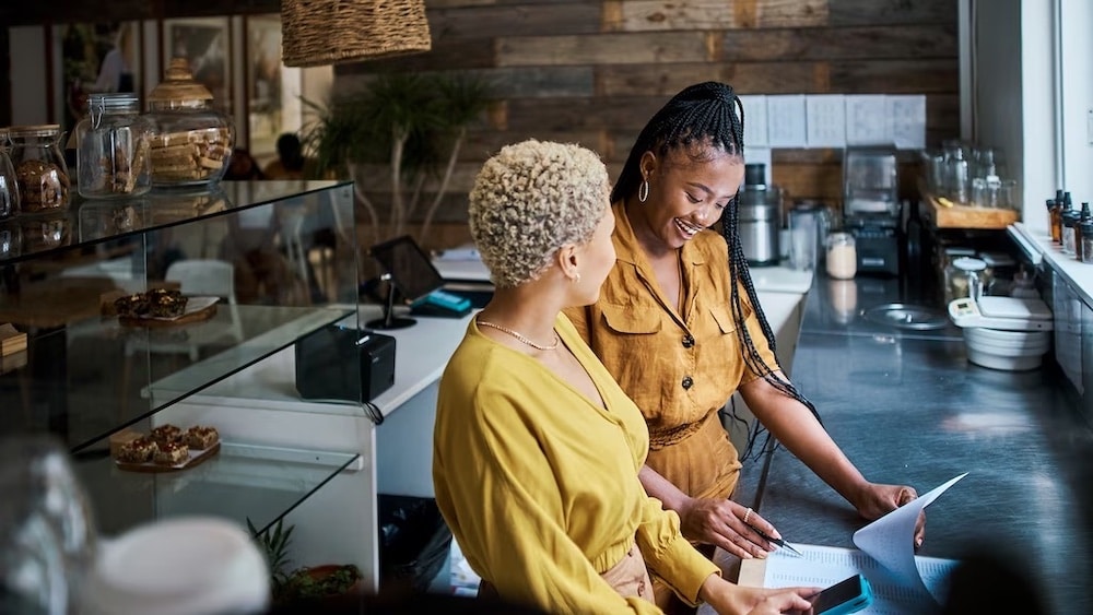 Two women looking at paperwork together behind restaurant counter
