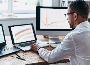 Person sitting at desk looking at laptop and computer monitors