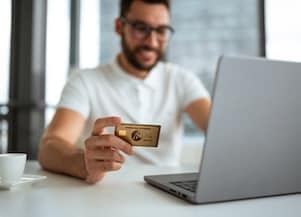 a person sitting at desk with laptop holding Amex card