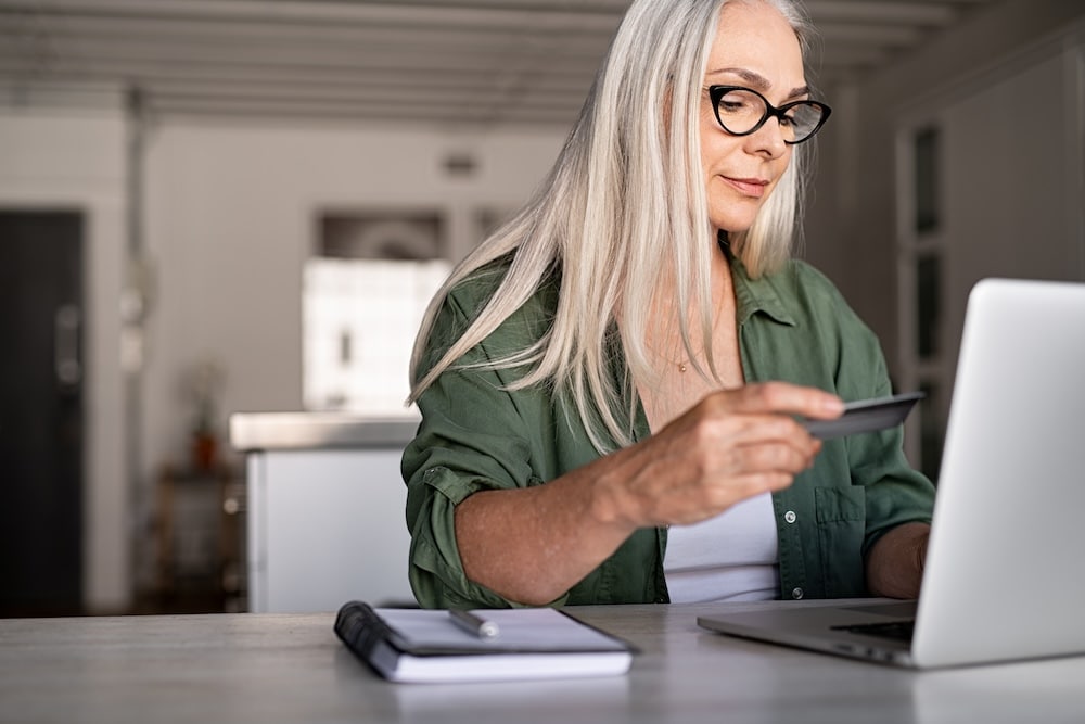 woman sitting at desk looking at laptop holding credit card