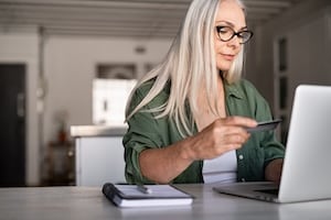 Woman sitting at desk with laptop holding credit card