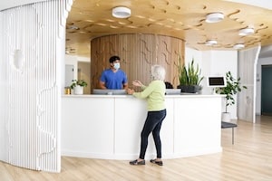 Woman at check-in desk speaking with a man, both wearing masks