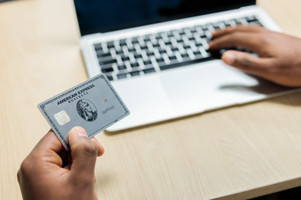 hand holding Amex card with laptop keyboard in background