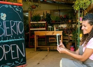 small business owner taking photo outside plant shop of chalkboard that says open