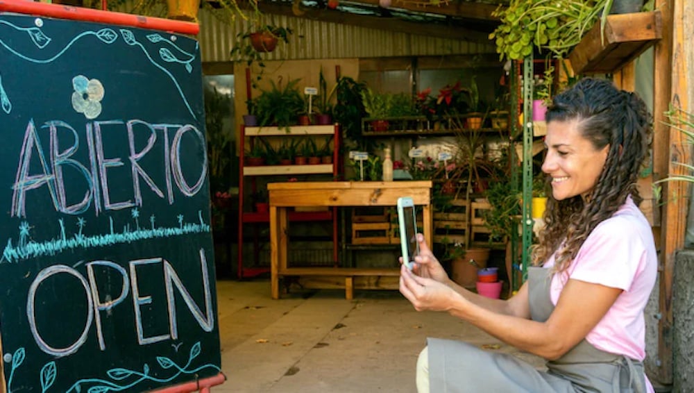 Plant shop owner taking photo of chalkboard sign that says "ABIERTO, OPEN"