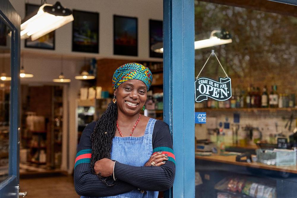 Small business owner standing in door with Come in, we are open sign in storefront window
