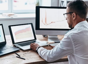 Man at a desk on laptop with monitors