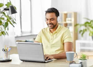 man at table looking at laptop with headphones on