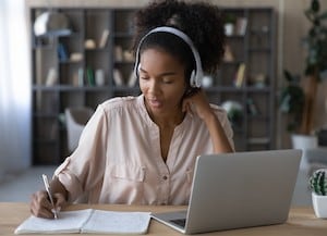 Woman writing in notebook on a desk by laptop