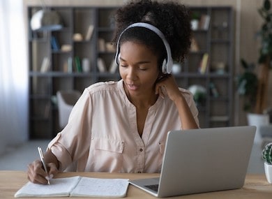 Woman writing in notepad at a desk with laptop